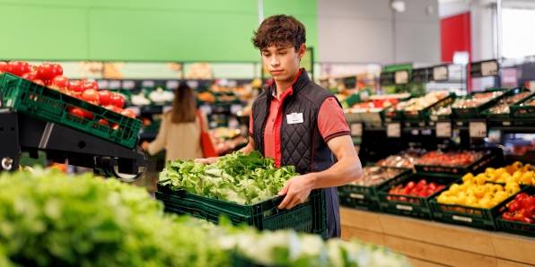 Obst- und Gemüsebereich einer Kaufland-Filiale: Junger Verkaufsmitarbeiter verräumt eine Box mit Salat.