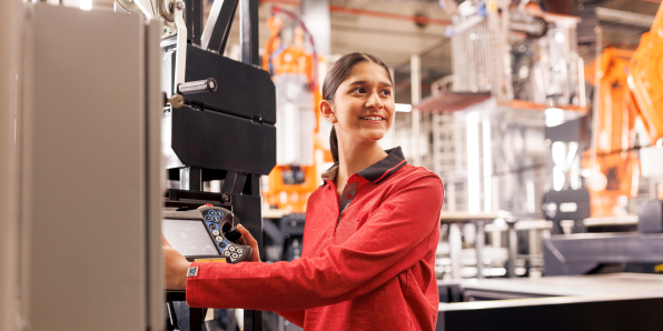 Eine Mitarbeiterin in rotem Pullover bedient eine Anlage bzw. eine Maschine.
