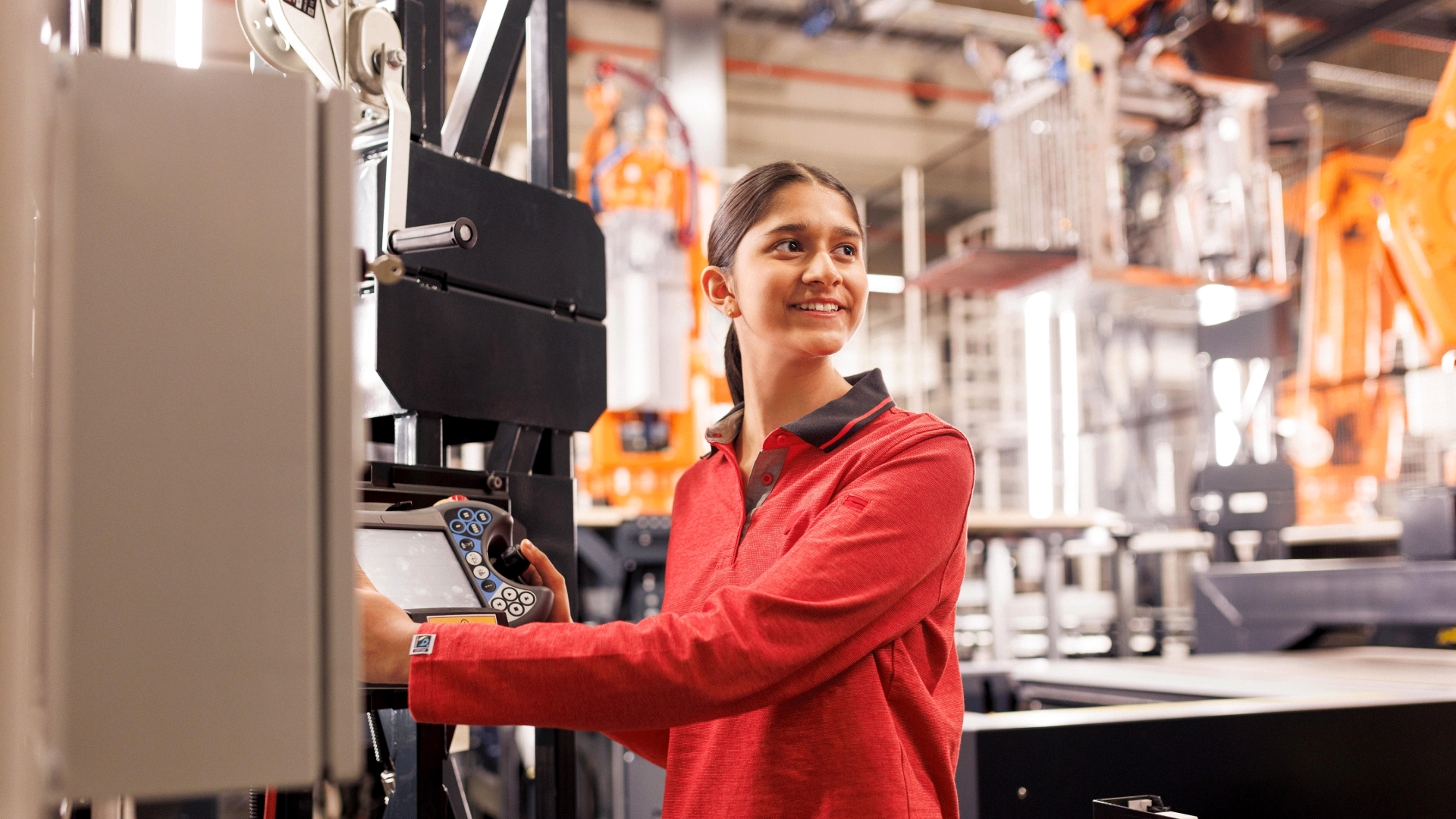 Eine Mitarbeiterin in rotem Pullover bedient eine Anlage bzw. eine Maschine.