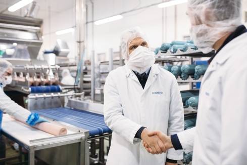 2 Mitarbeiter im Kaufland-Fleischwerk begrüßen sich in der Produktion.