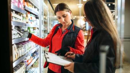 2 Kaufland-Verkaufsmitarbeiterinnen am Kühlregal. Eine Kollegin scannt die Ware, die andere gleicht Ware und Preise anhand einer Liste ab.