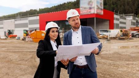 Zwei Bauleiter stehen vor dem Bau eines Kaufland-Marktes und sprechen über einen Bauplan, den sie in den Händen halten.